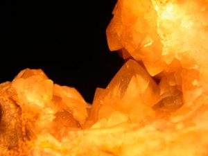 Bright orange quartz crystals with a black background visible in the upper left quarter of the image