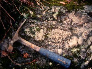 A rock hammer is on the bottom right of the amblygonite outcrop image.
