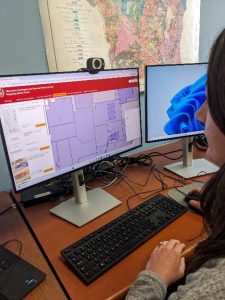 Amy sits at a desktop computer, browsing the WGNHS Mapping Status Portal