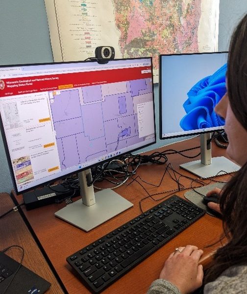 Amy sits at a desktop computer, browsing the WGNHS Mapping Status Portal