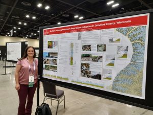 Woman with brown hair standing next to scientific poster in large conference hall.