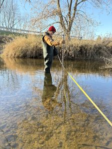 Woman in waders standing in a stream.