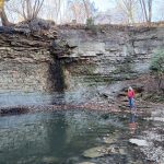 Woman in a jacket overlooking clear waters with limestone outcrop in the background.